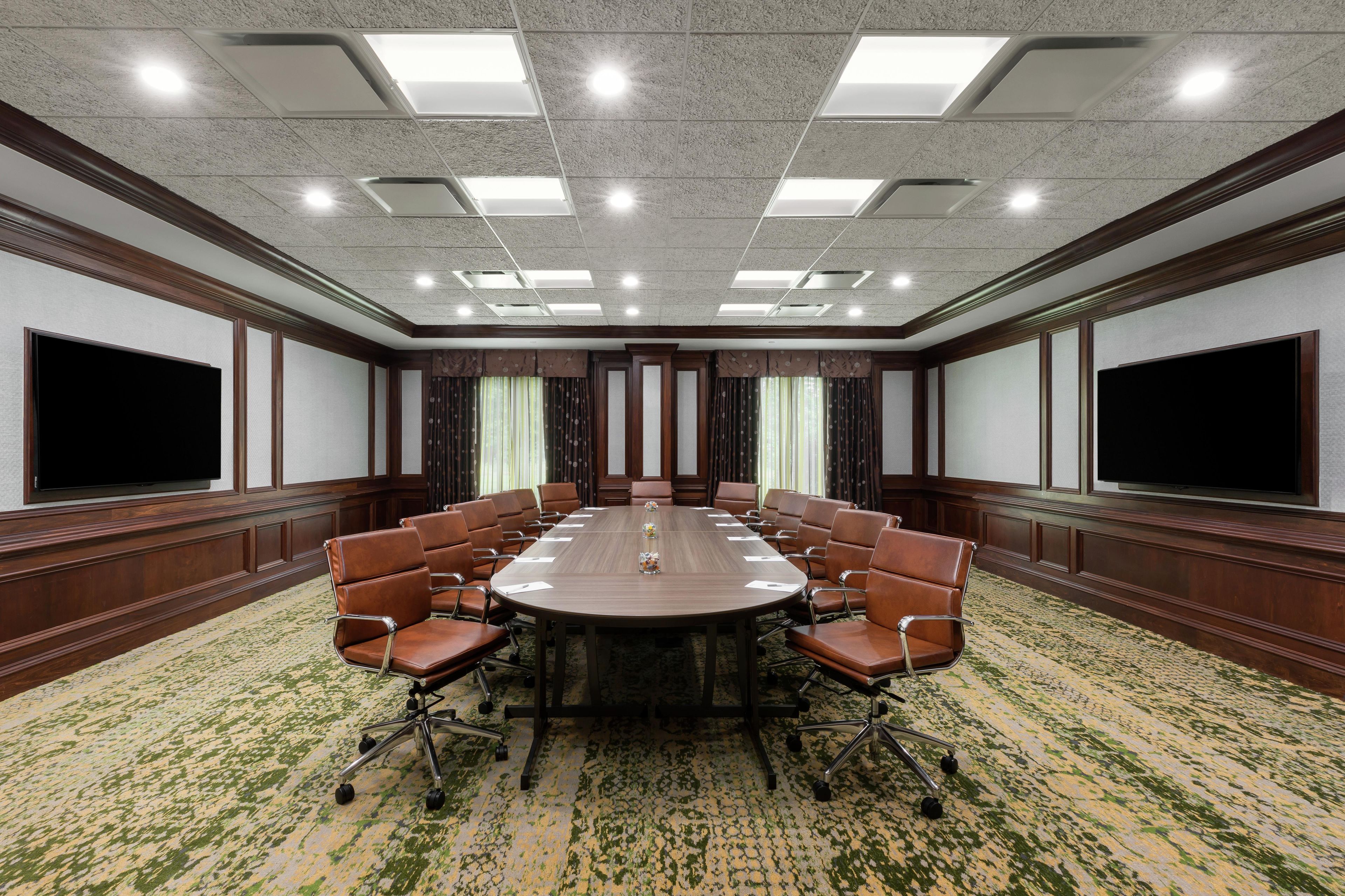 Une salle de conférence dotée d’une grande table ovale, de fauteuils en cuir marron, d’un sol recouvert de moquette et d’un plafond pourvu d’un éclairage encastré.