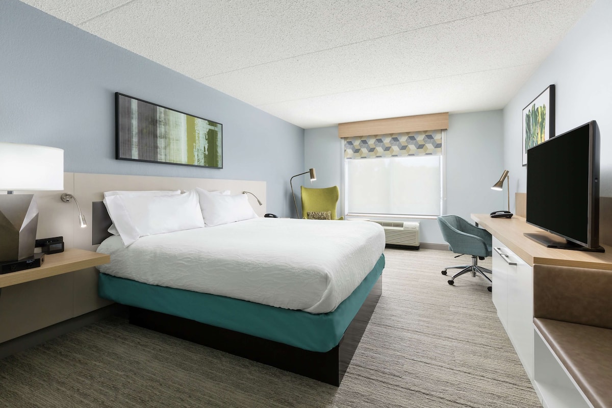 A hotel room with a bed, a desk with a computer, a TV, and a chair.