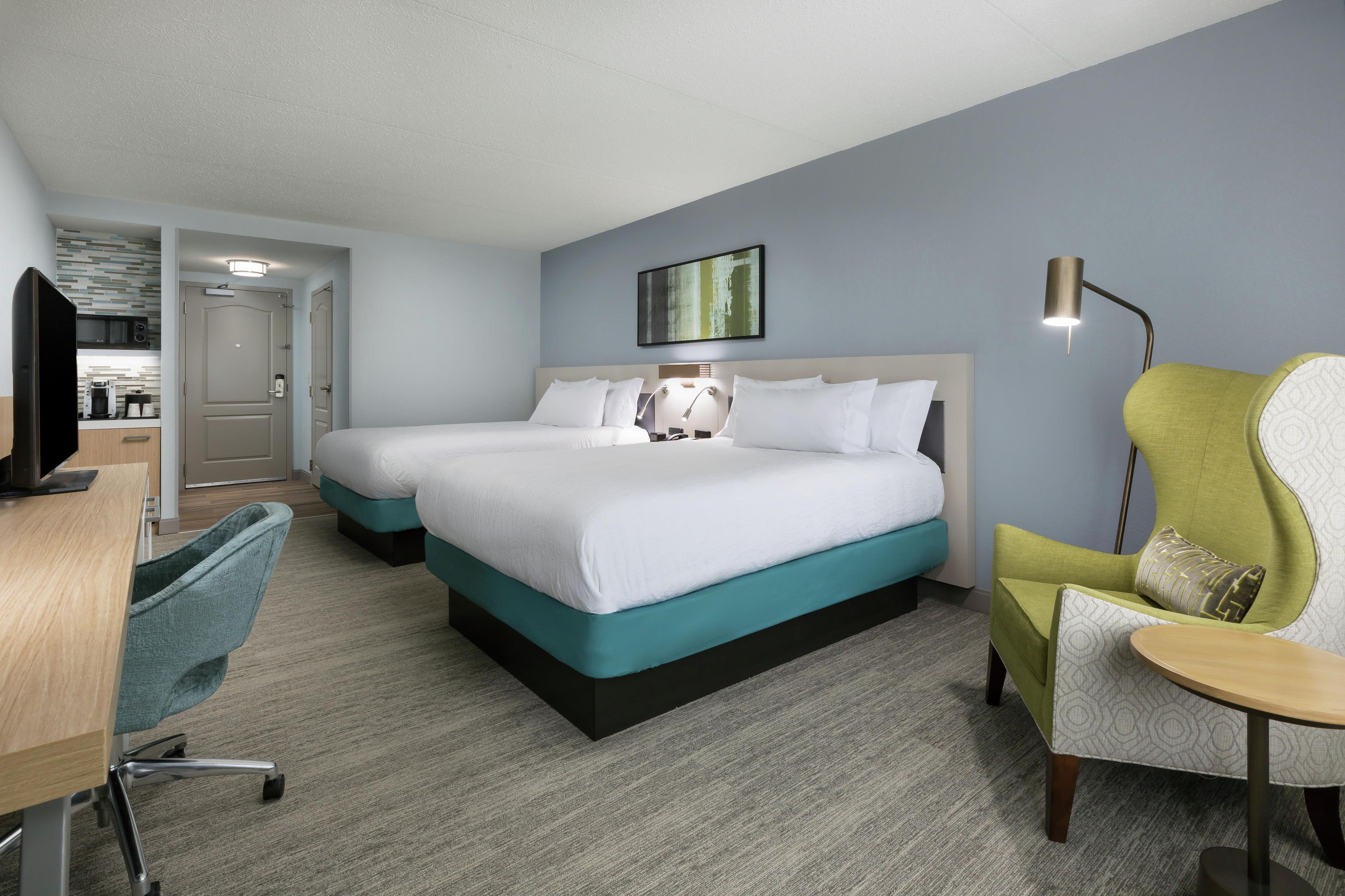 A hotel room with a double bed, a desk with a chair, a television, and a kitchenette.