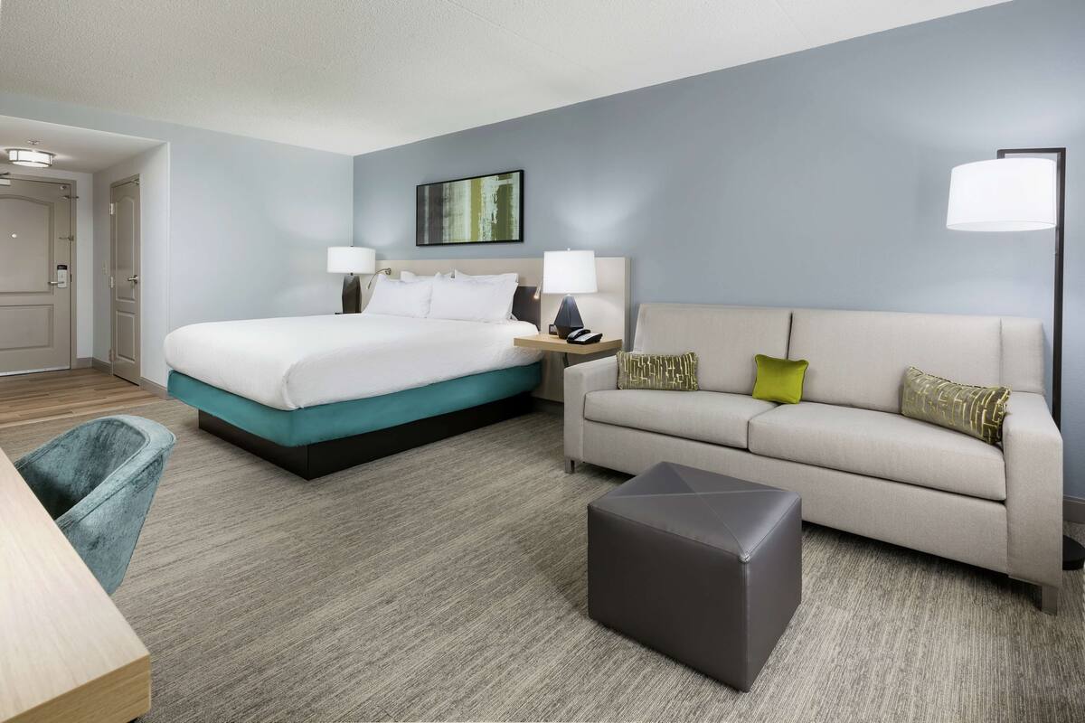 A hotel room with a bed, a sofa, a coffee table, and a desk.