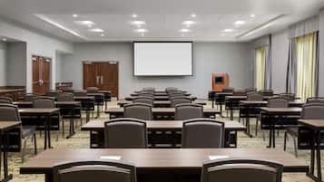 A conference room with multiple tables and chairs, a projector screen, and a podium.