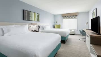 Une chambre d’hôtel avec deux lits, un bureau, une chaise, une télévision et une fenêtre avec des stores.