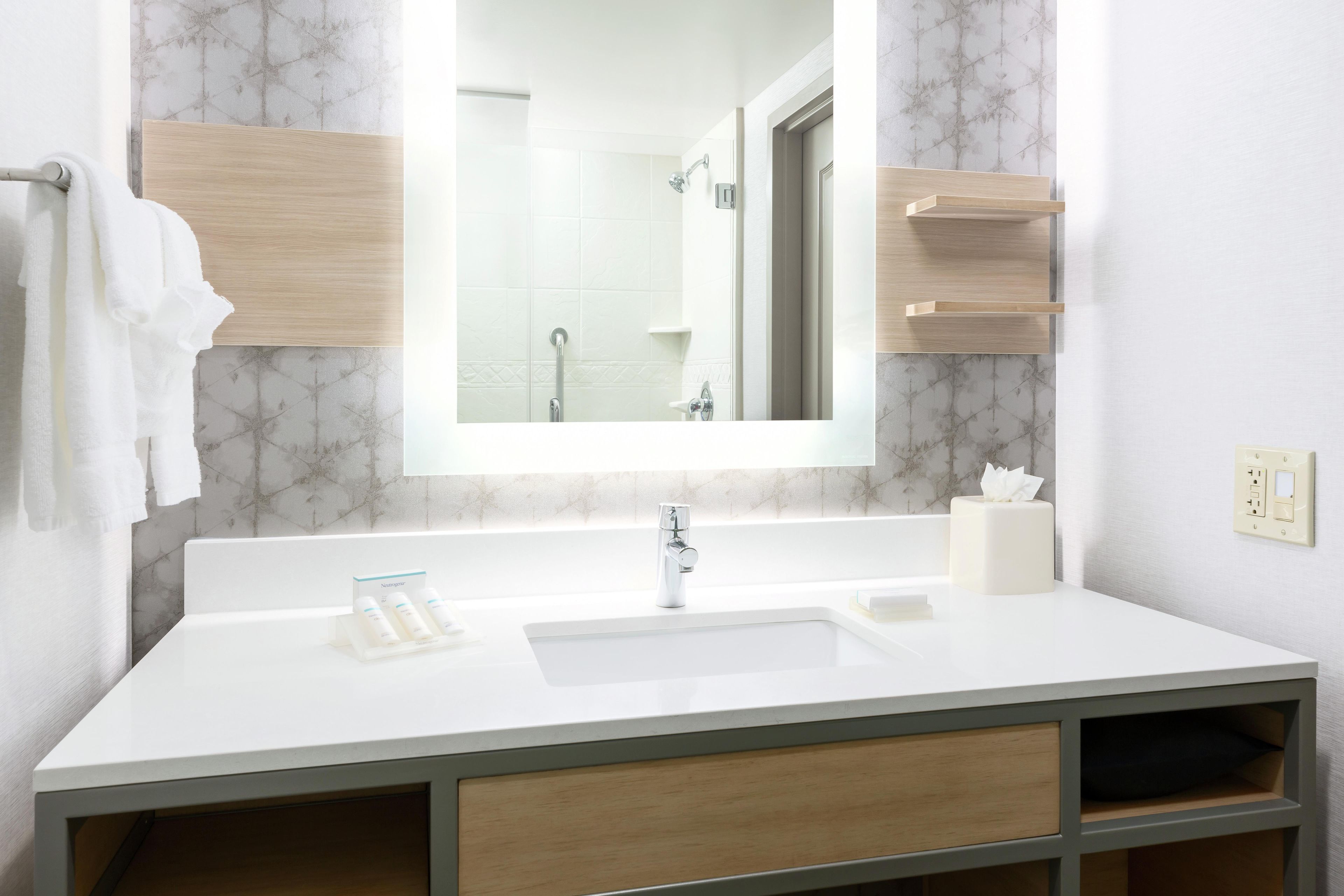 A bathroom with a white sink, a mirror, a shower, and a towel rack.