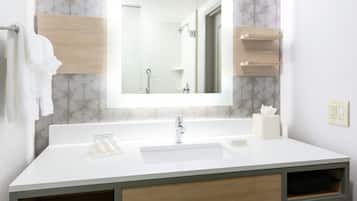 A bathroom with a white sink, a mirror, a shower, and a towel rack.