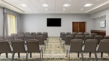 Une salle de conférence avec des rangées de chaises, un téléviseur à écran plat, une porte et un sol recouvert de moquette.