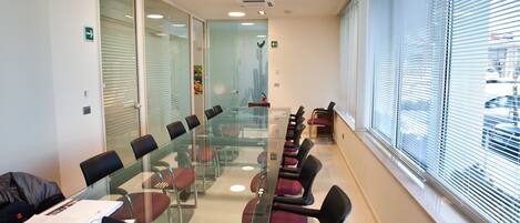 Un salón de conferencias con una mesa de vidrio, sillas rojas y un ordenador portátil sobre la mesa.