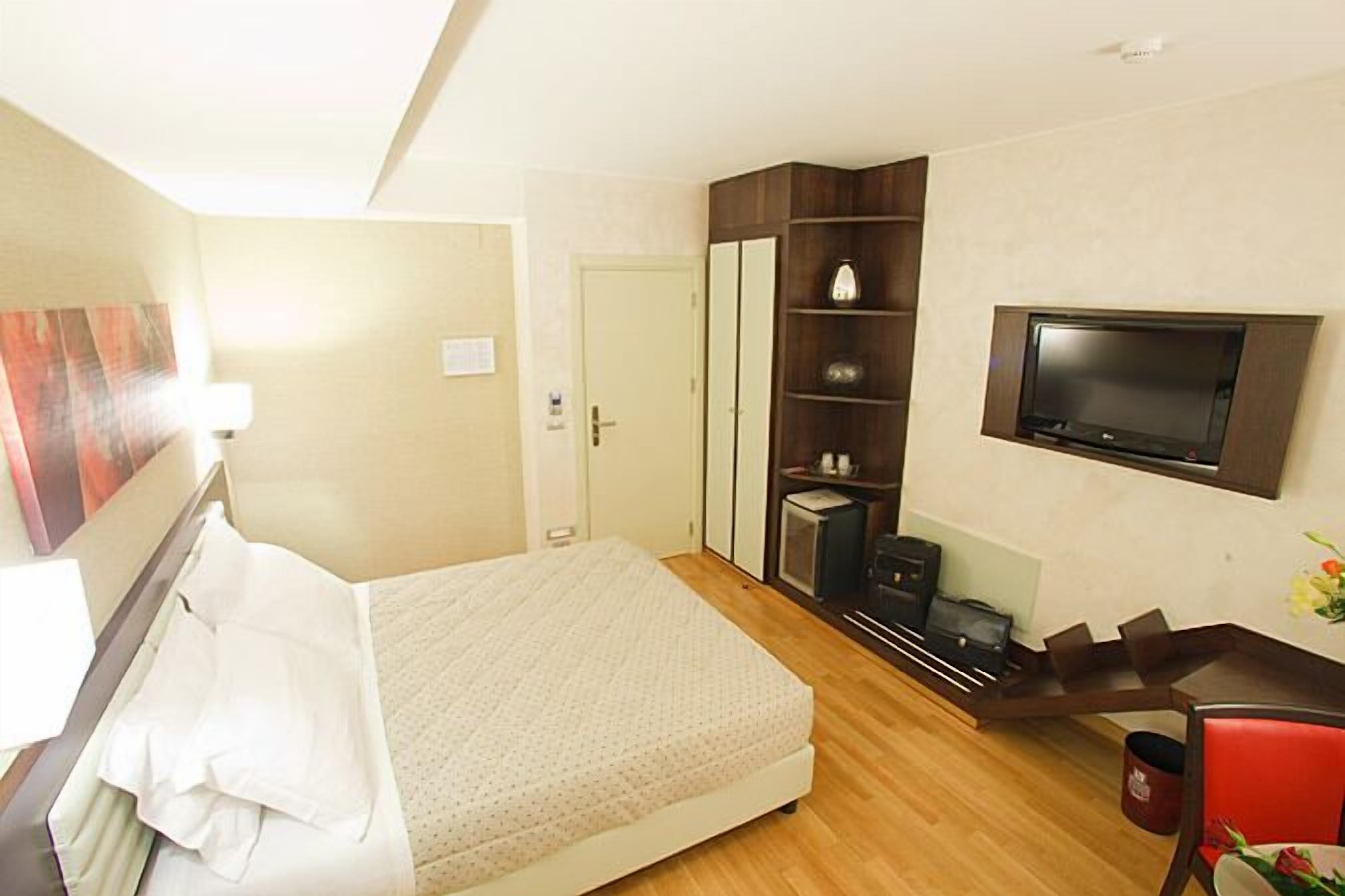 Habitación de hotel con cama, escritorio con silla, televisión, armario y puerta.