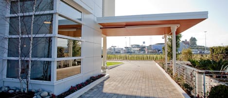 A modern building with large windows, a paved walkway, and a view of a parking area.