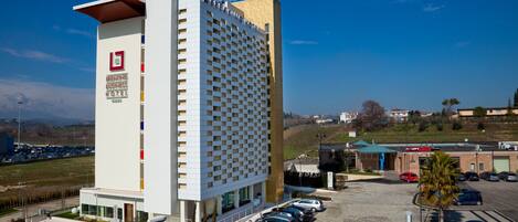 A modern hotel with a prominent sign, a parking lot, and a view of the surrounding landscape.