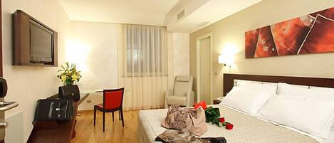 A hotel room with a bed, a desk with a chair, a television, and a painting on the wall.