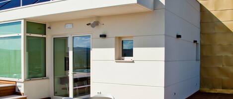 A modern outdoor deck with white wicker furniture and a glass door entrance.
