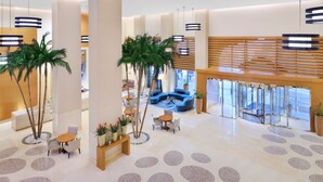 A spacious lobby with a central seating area, palm trees, and a modern ceiling design. - Mövenpick Hotel Jumeirah Beach (Dubai)