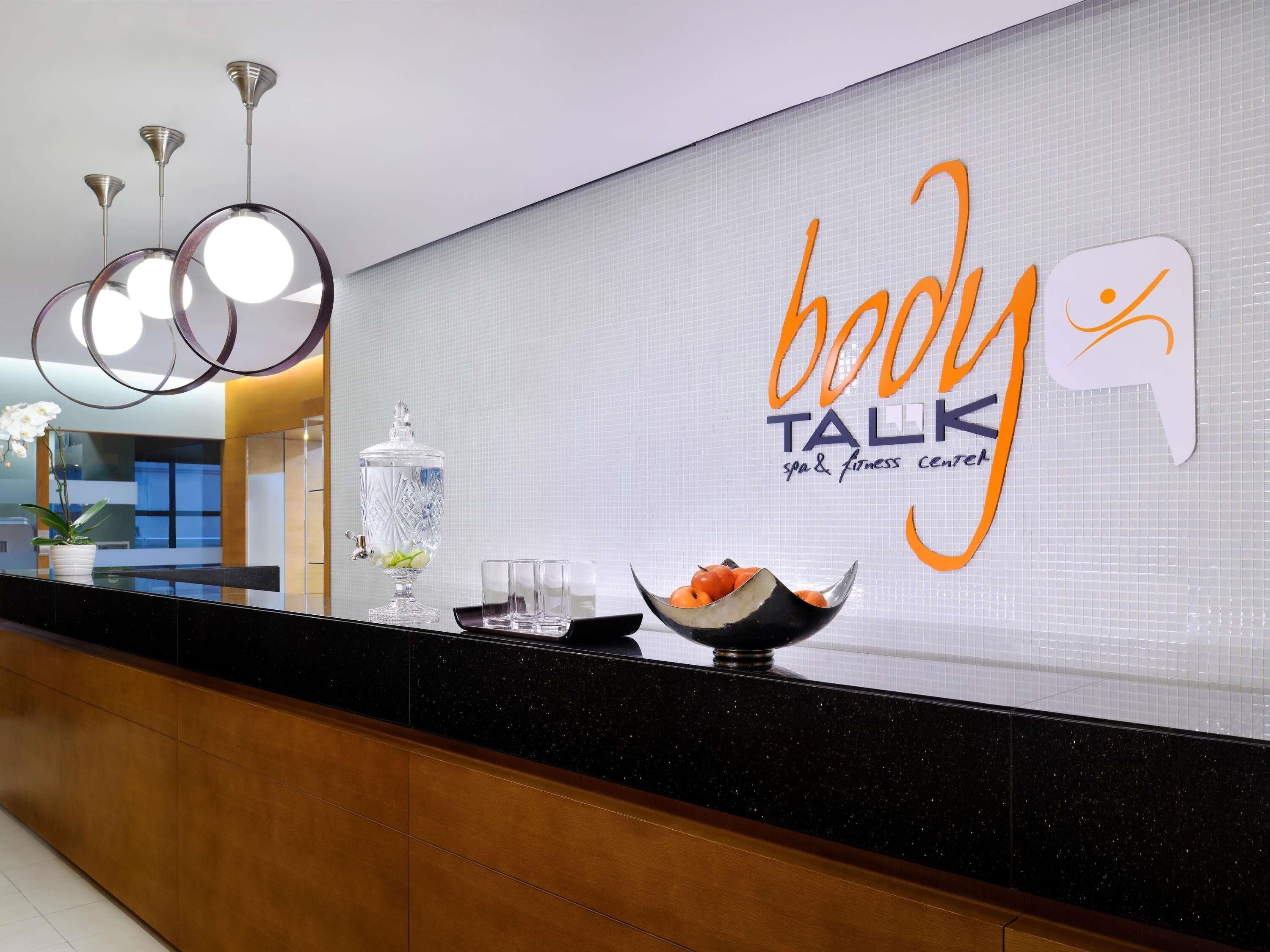 Ein Empfangsbereich mit einem Schild für das 'body TALK spa & fitness center', einer dekorativen Vase und einer Obstschale.
