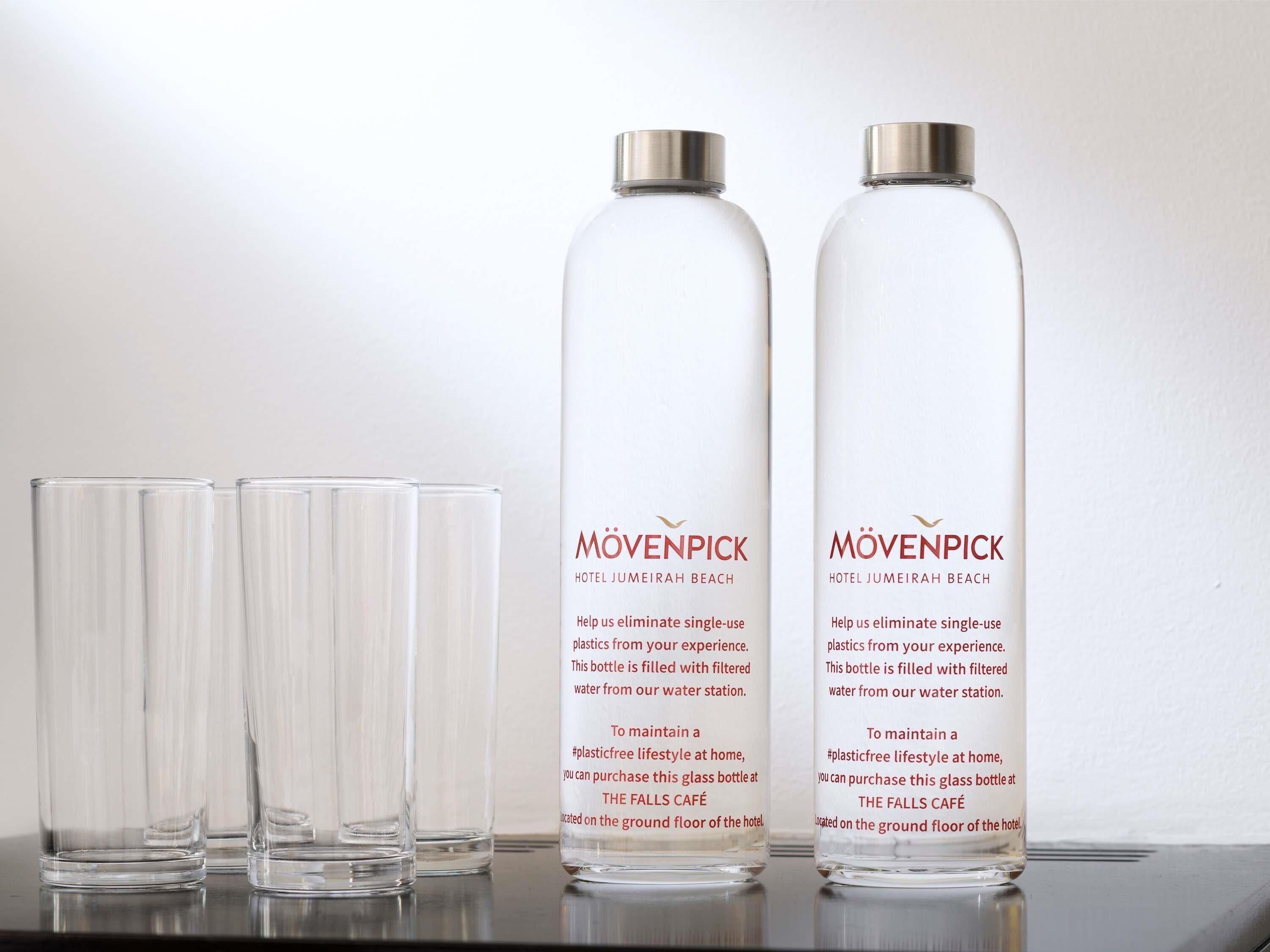 Trois bouteilles en verre transparent et trois verres en verre transparent, posés sur une surface réfléchissante.