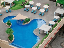 A rooftop pool area with blue water, lounge chairs, and umbrellas.