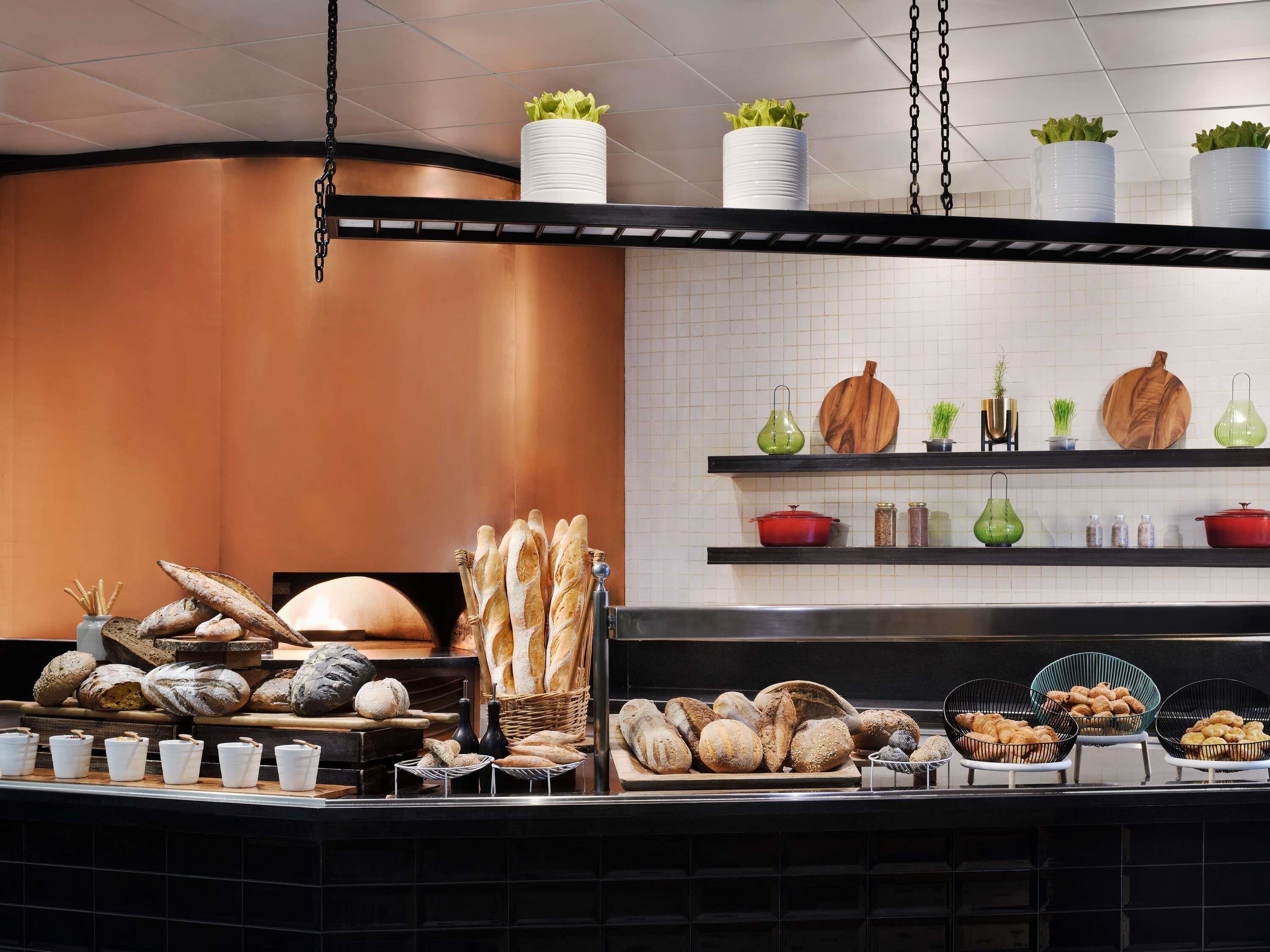 Een bakkerij etalage met verschillende broden en gebak, planken met keukengerei en hangplanten.