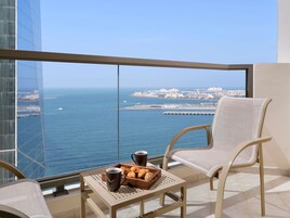 A balcony with a table set for breakfast, a chair, and a view of the sea and cityscape.
