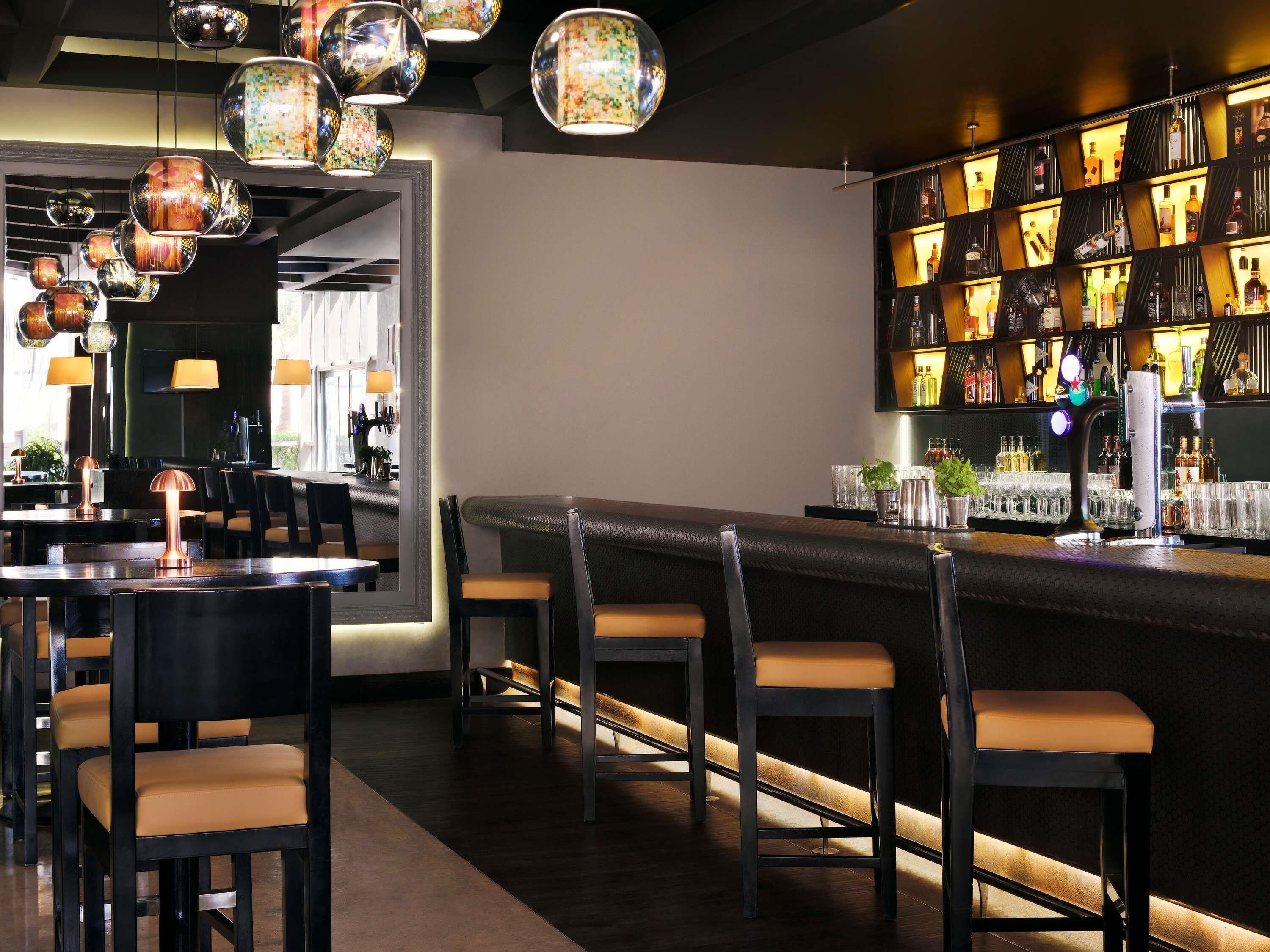 A bar area with multiple seating options, a well-lit bar counter, and a variety of bottles and glasses.