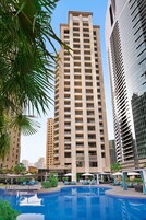 A swimming pool with lounge chairs and umbrellas, surrounded by tall buildings.