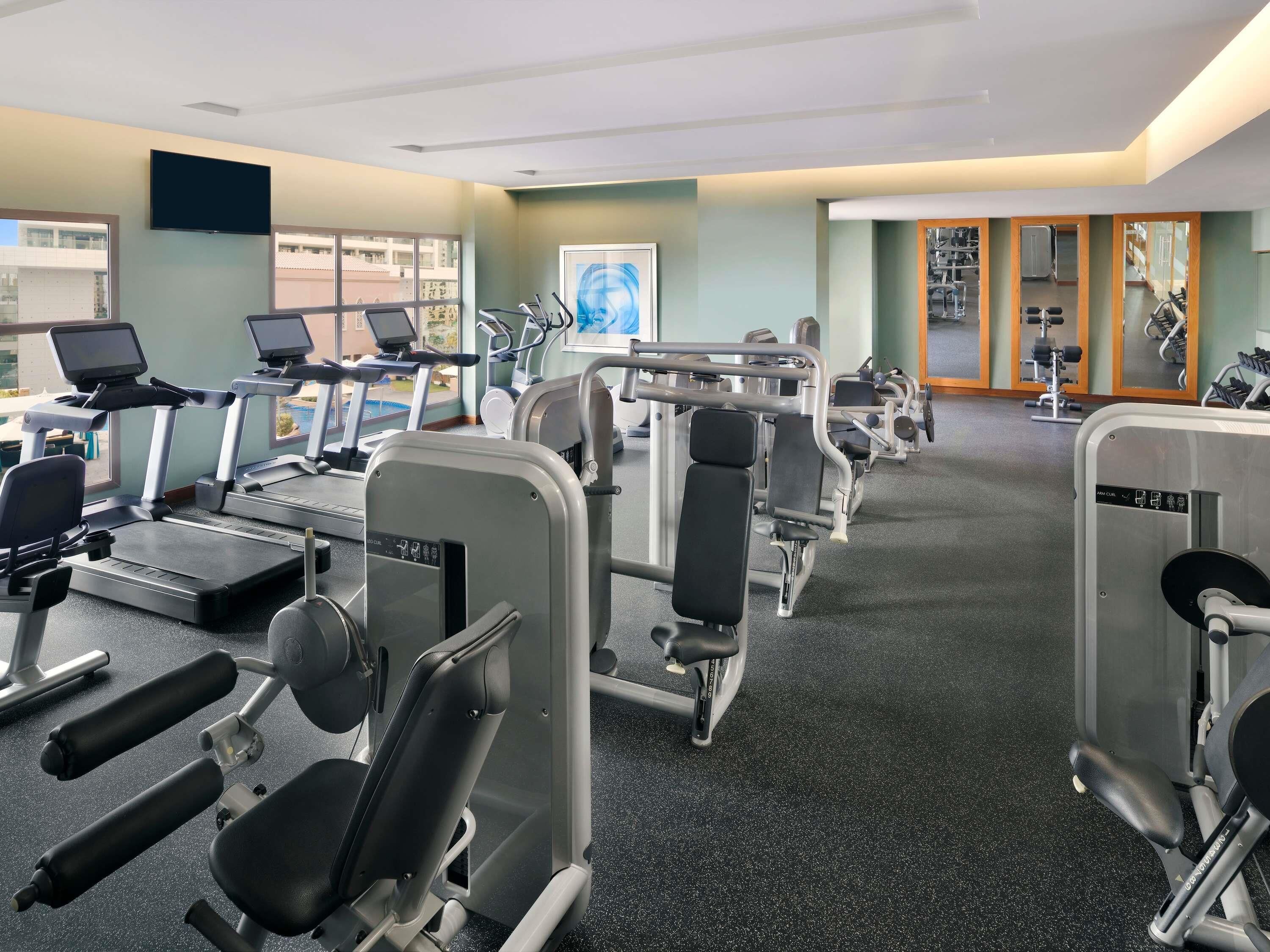 Une salle de sport équipée de tapis de course, d’appareils de musculation et d’un mur recouvert de miroirs.