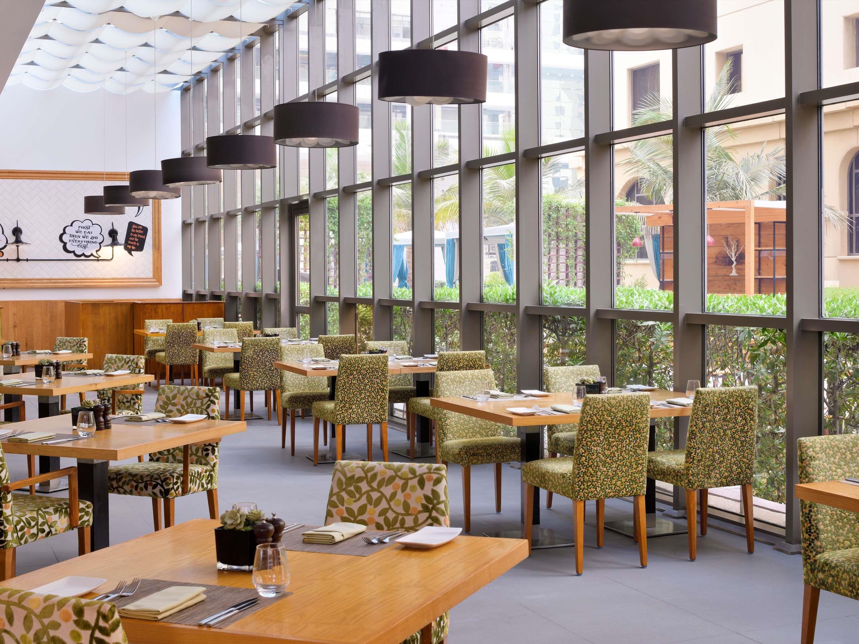 Un restaurant moderne doté de grandes fenêtres, de chaises à motifs et de tables en bois.