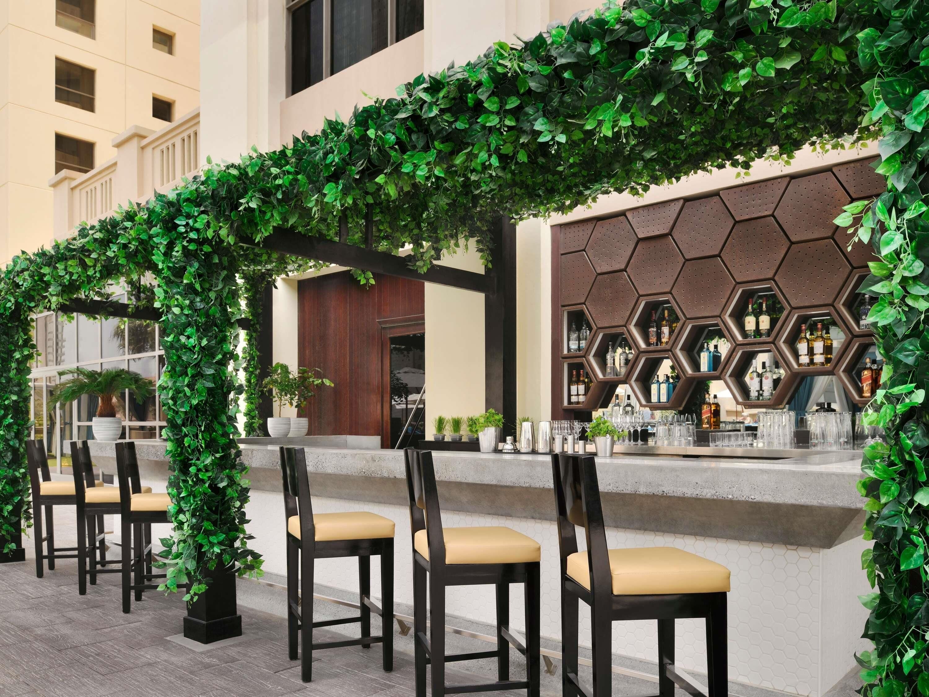 An outdoor seating area with a green archway, bar counter, and chairs.
