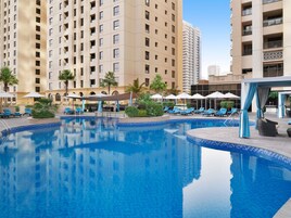A swimming pool with lounge chairs and umbrellas, surrounded by tall buildings.