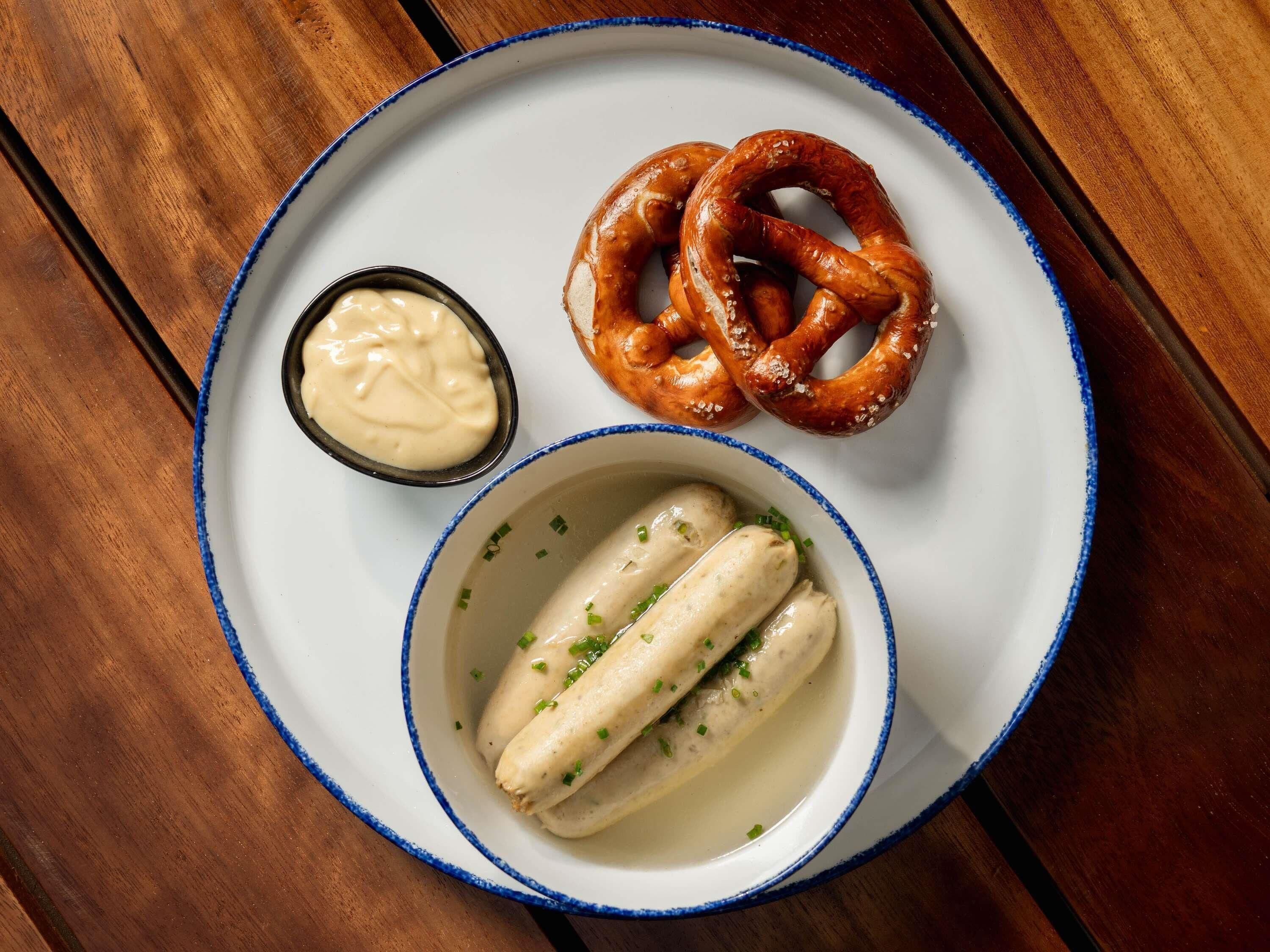 A plate with pretzels, a small bowl of sauce, and two boiled eggs garnished with chives.
