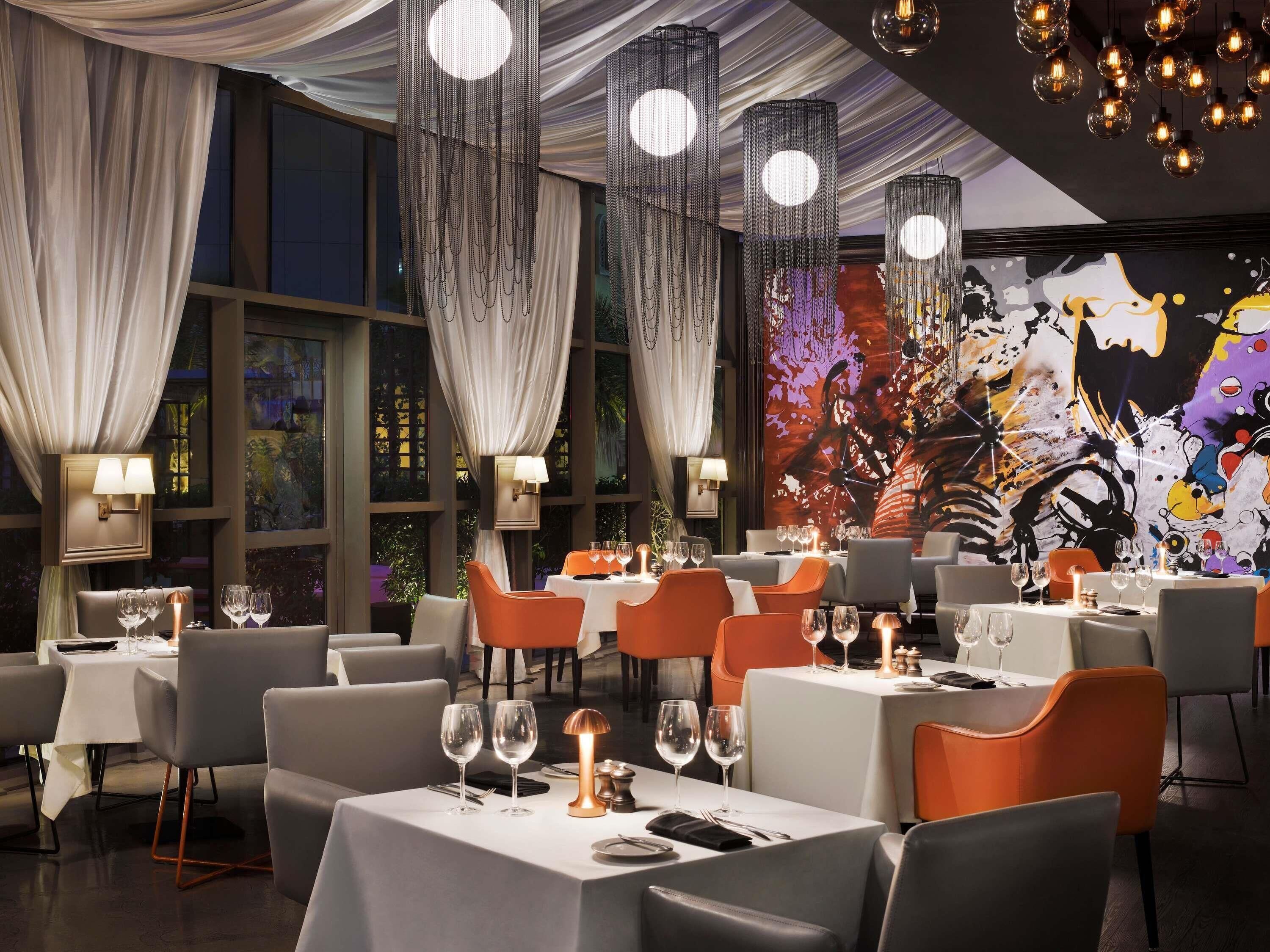 A restaurant with tables set for dining, ambient lighting, and a large mural on the wall.