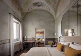 A bedroom with a large bed, a desk, a chair, and a window with curtains.