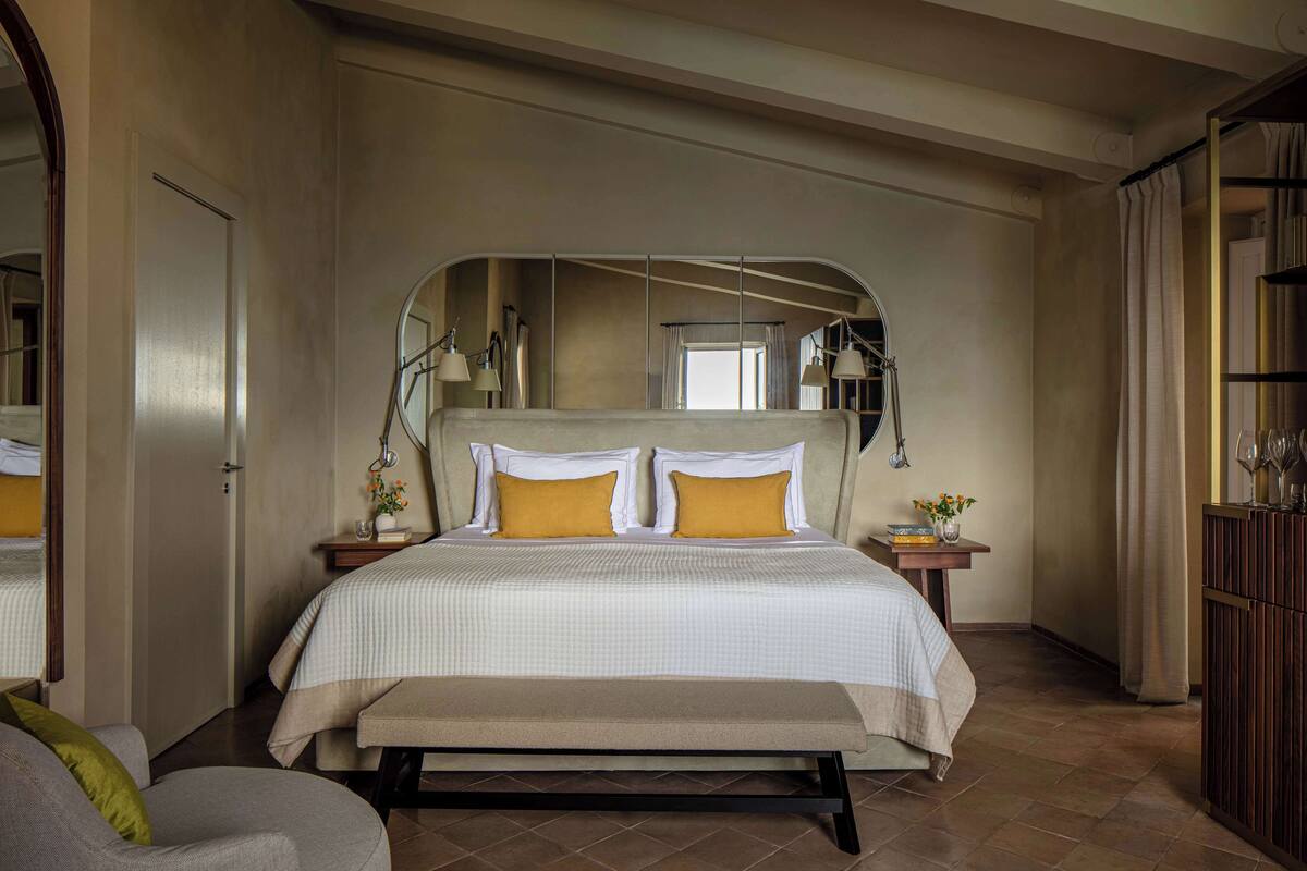 Een slaapkamer met een bed, een bankje, een nachtkastje, een spiegel en een kledingkast.