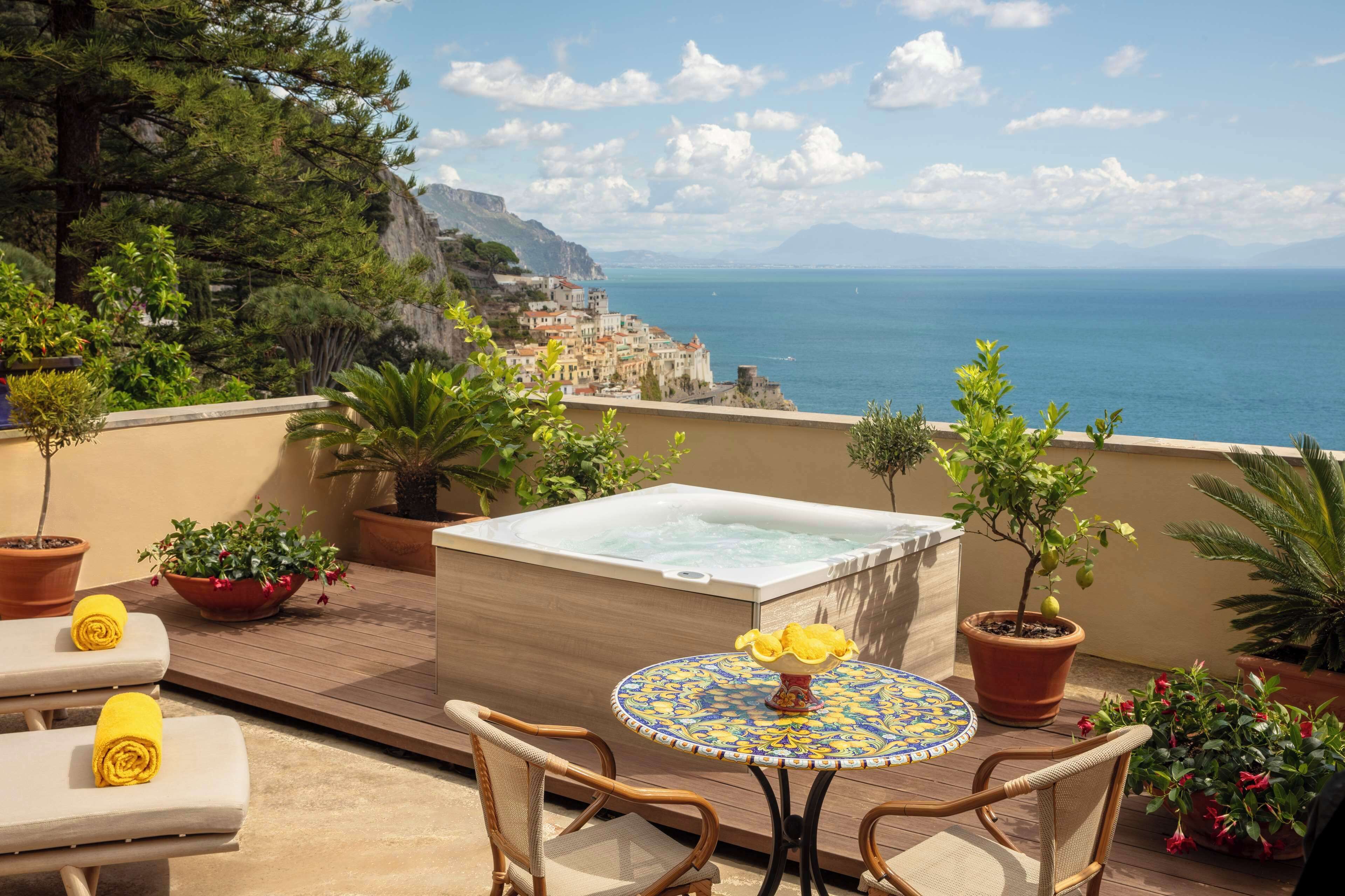 A balcony with a hot tub, lounge chairs, and potted plants.