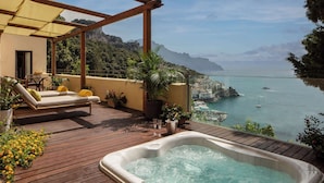 A wooden deck with a hot tub, lounge chairs, and a view of the sea.