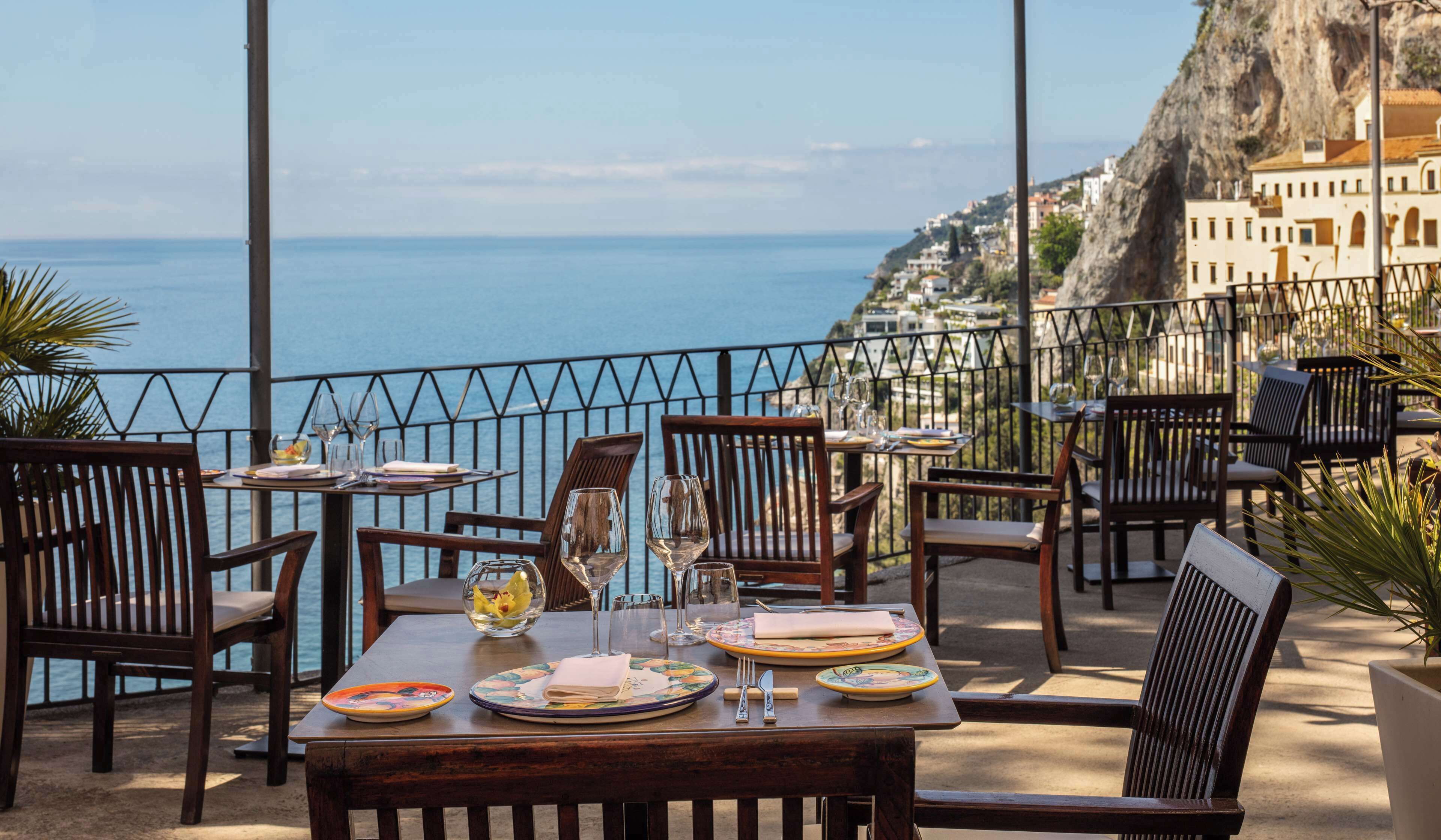 Mesa dispuesta para comer con vista al mar y a un pueblo en el acantilado.