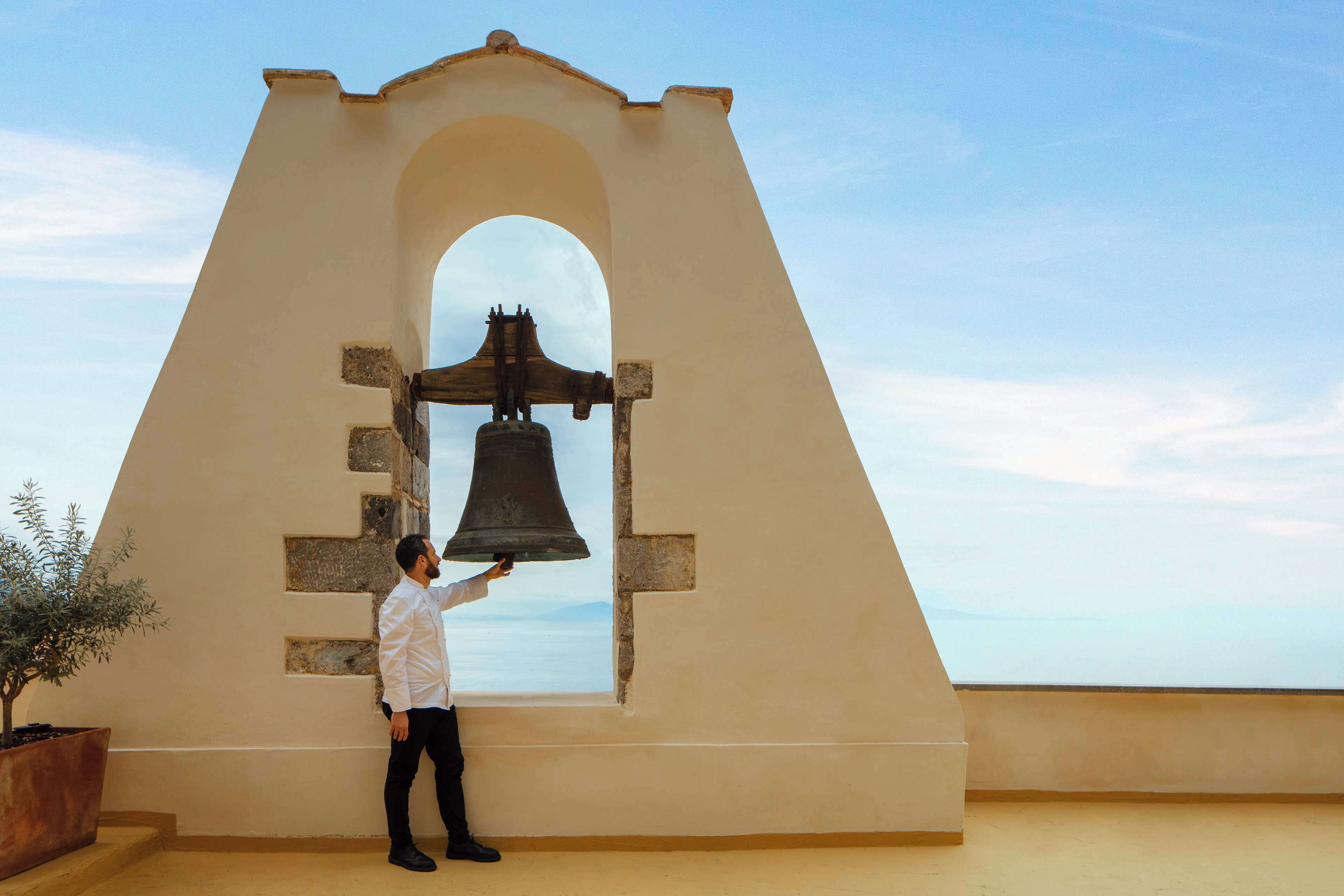 Una persona tocando una campana ubicada en una estructura con ventanal de arco.