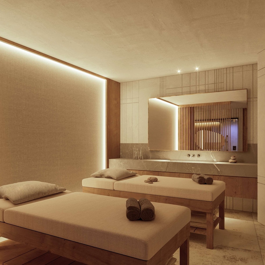 A modern spa room with a wooden bench, a massage table, and a large mirror above a vanity.