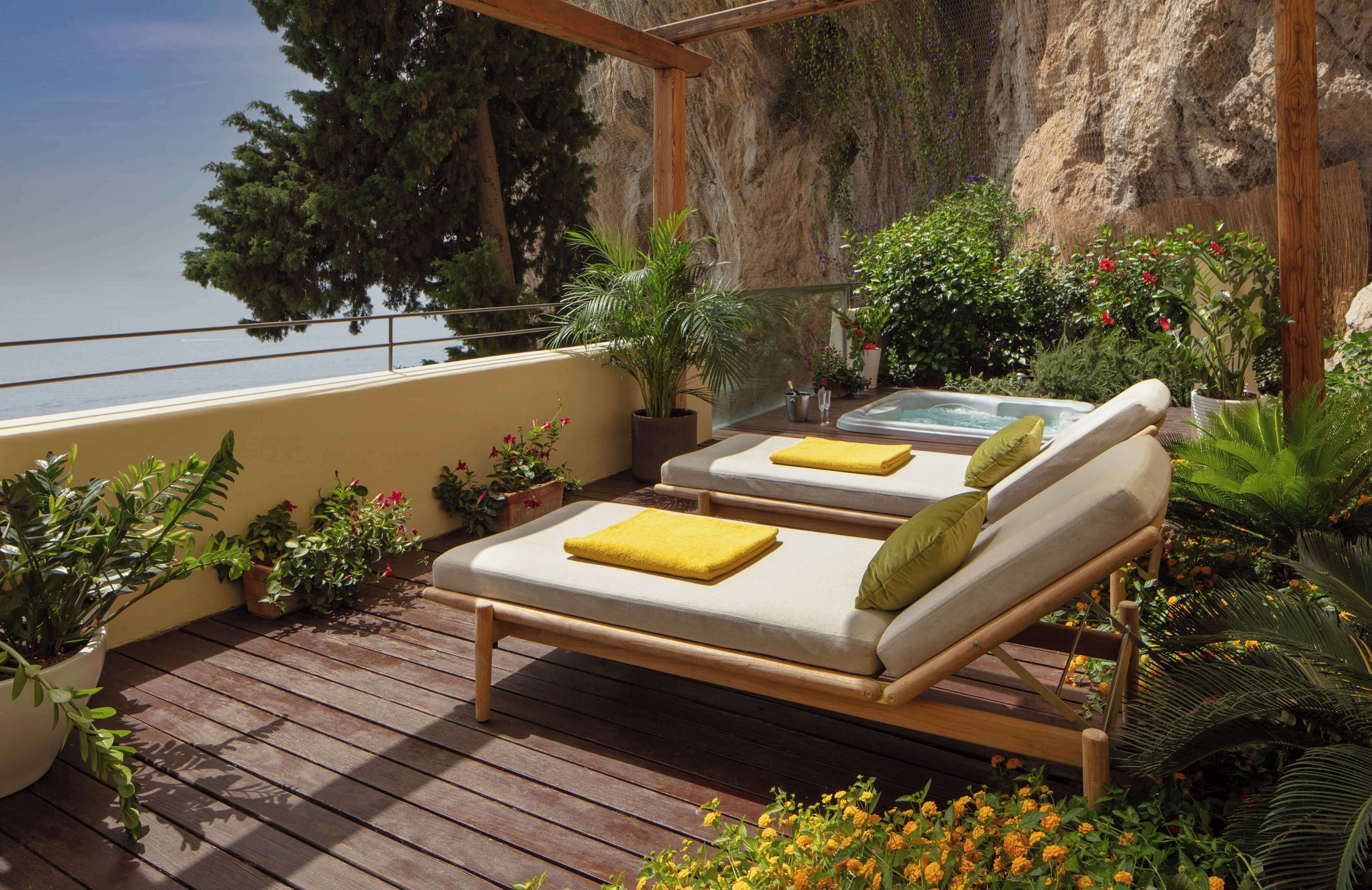 A wooden deck with two lounge chairs, a hot tub, and potted plants.