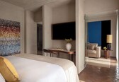 A hotel room with a bed, a small table with a vase, a sofa, and a TV.