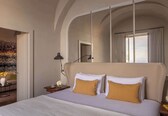 A hotel room with a large bed, a nightstand, a lamp, a window with curtains, and a view of the city.