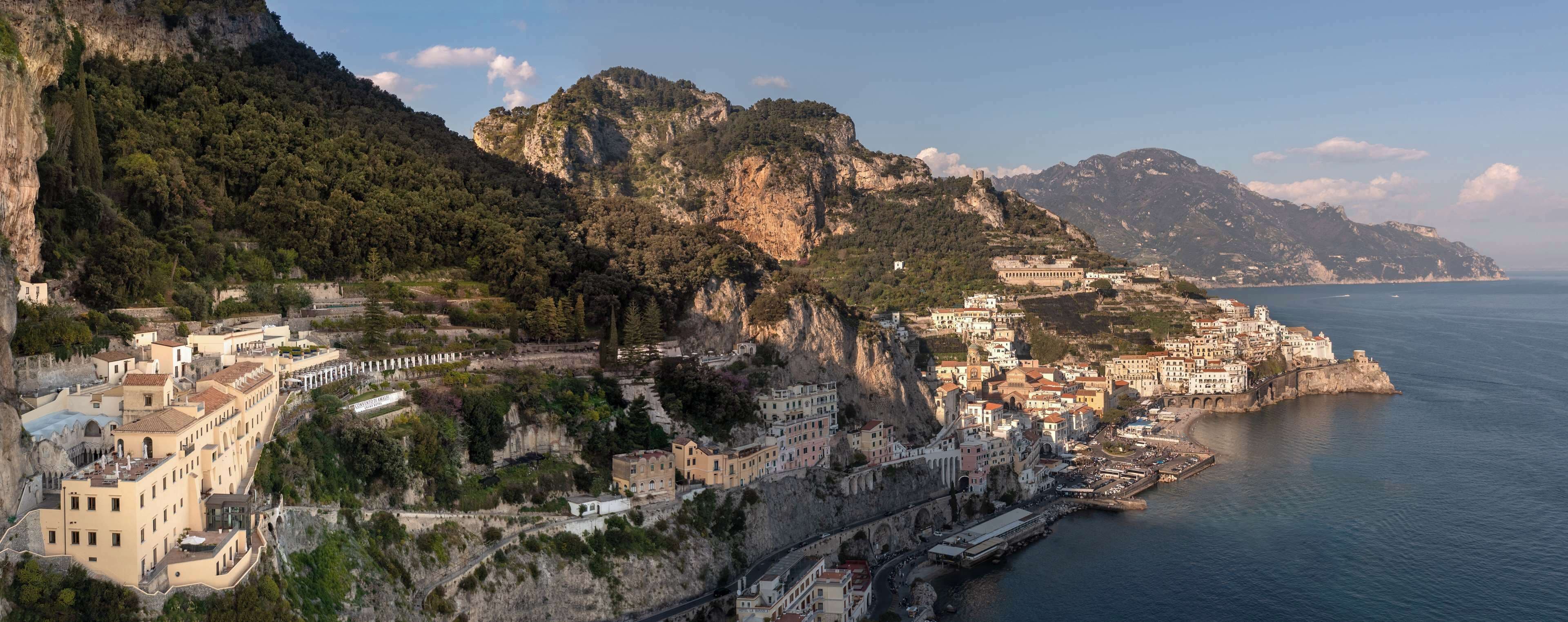 A coastal town with buildings built into the hillside, a harbor, and a mountainous backdrop.