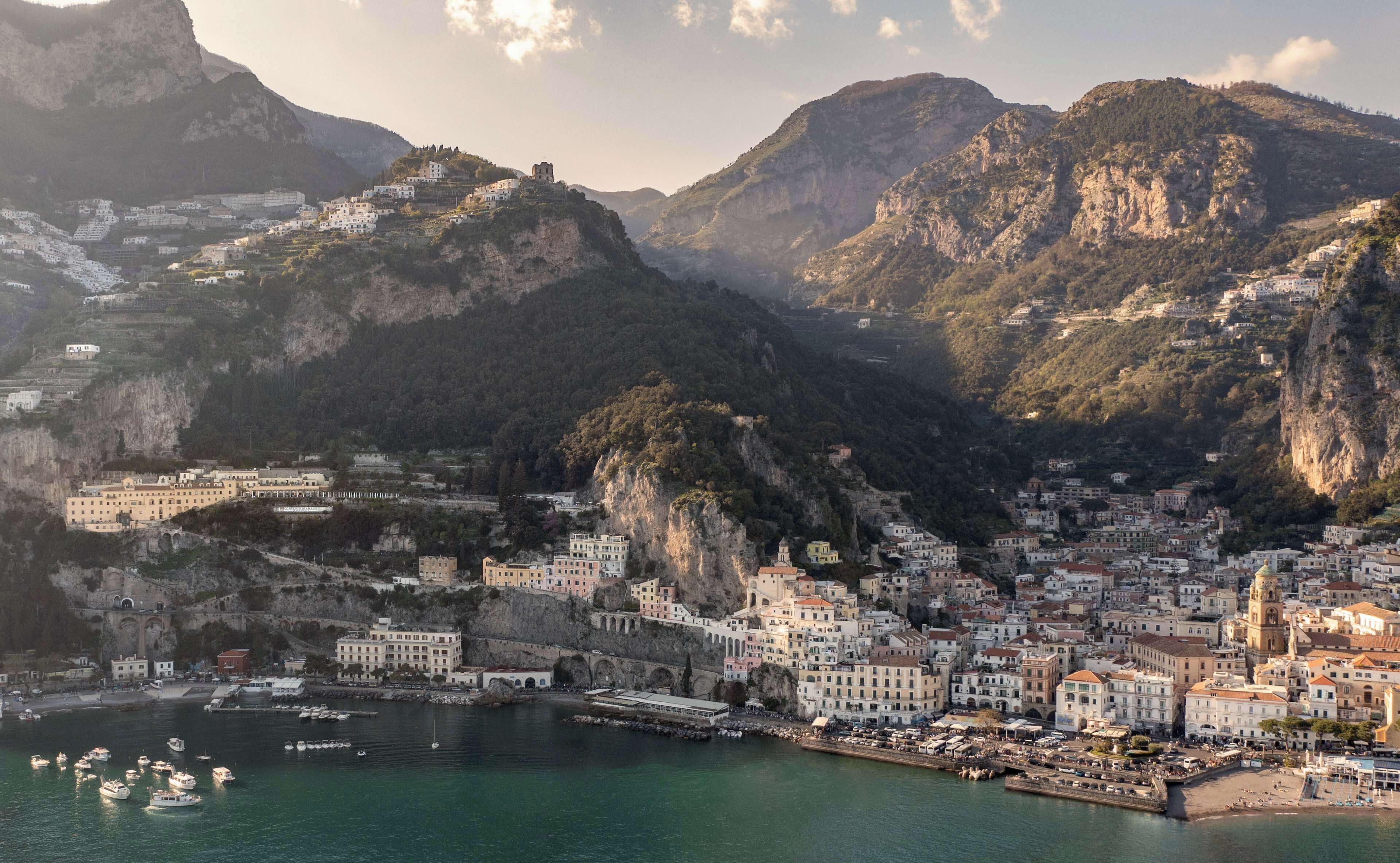 Une ville côtière avec des bâtiments construits sur une colline, un port de plaisance rempli de bateaux et un clocher d’église imposant.