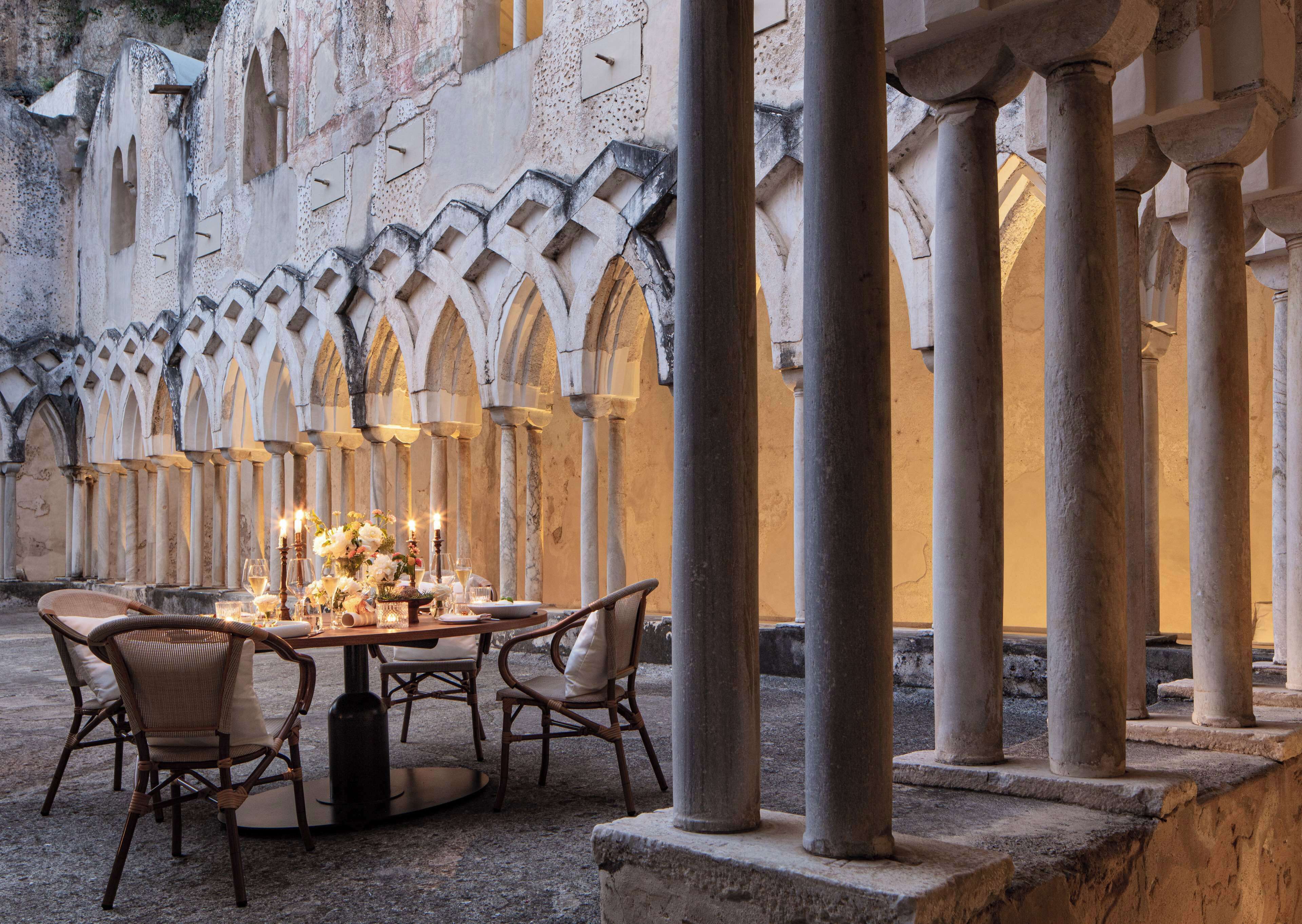 A dining area with a table set for four, surrounded by stone columns and arches.