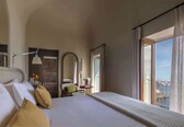 A hotel room with a bed, a chair, a table, a mirror, and a balcony with a view.