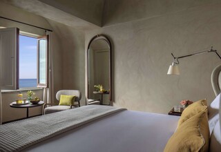 A hotel room with a bed, a chair, a small table with a vase and a lamp, and a large mirror.
