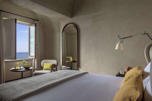 A hotel room with a bed, a chair, a small table with a vase and a lamp, and a large mirror.