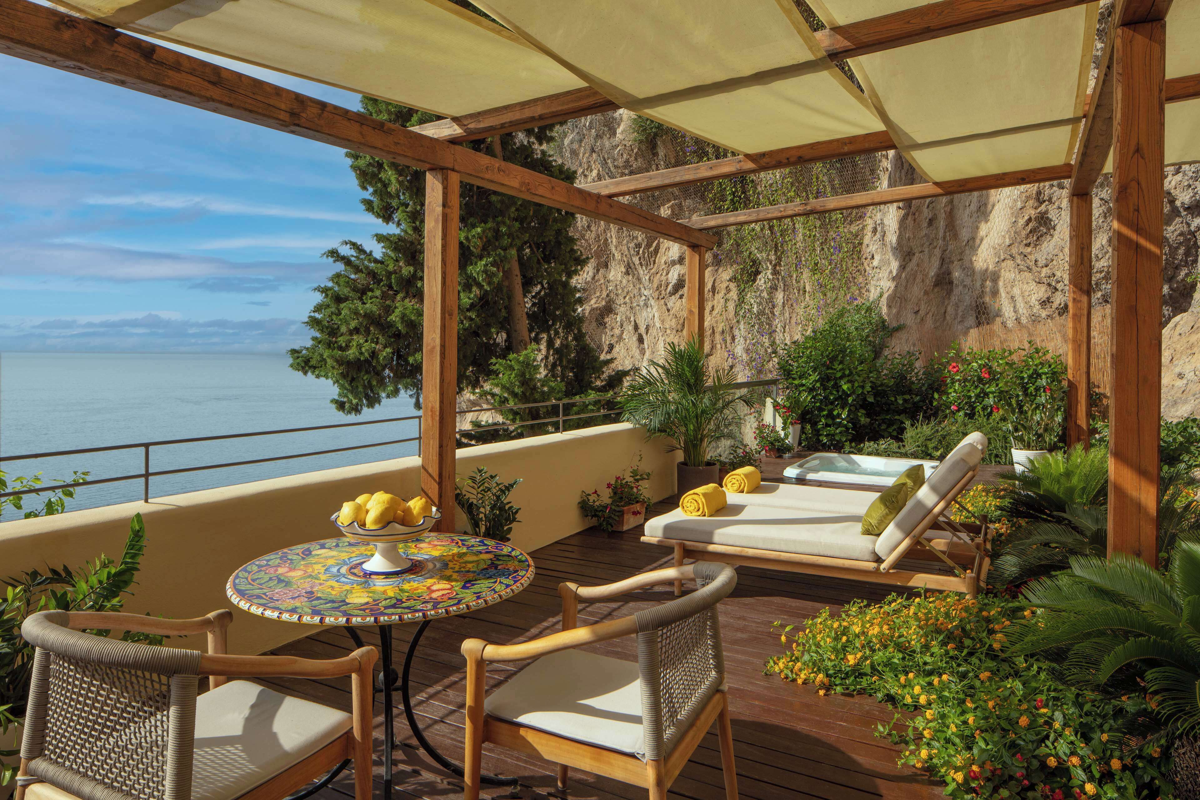 A wooden deck with a table, chairs, and a lounge area overlooking a body of water.