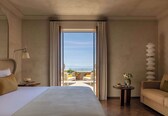 A hotel room with a large bed, a sofa, a small table with a vase, and a view of the balcony.