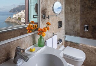 A bathroom with a view of a coastal town, a sink, a toilet, a mirror, and a shower.