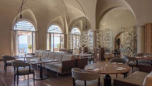 A spacious dining area with high arched ceilings, multiple seating arrangements, and large windows providing views.