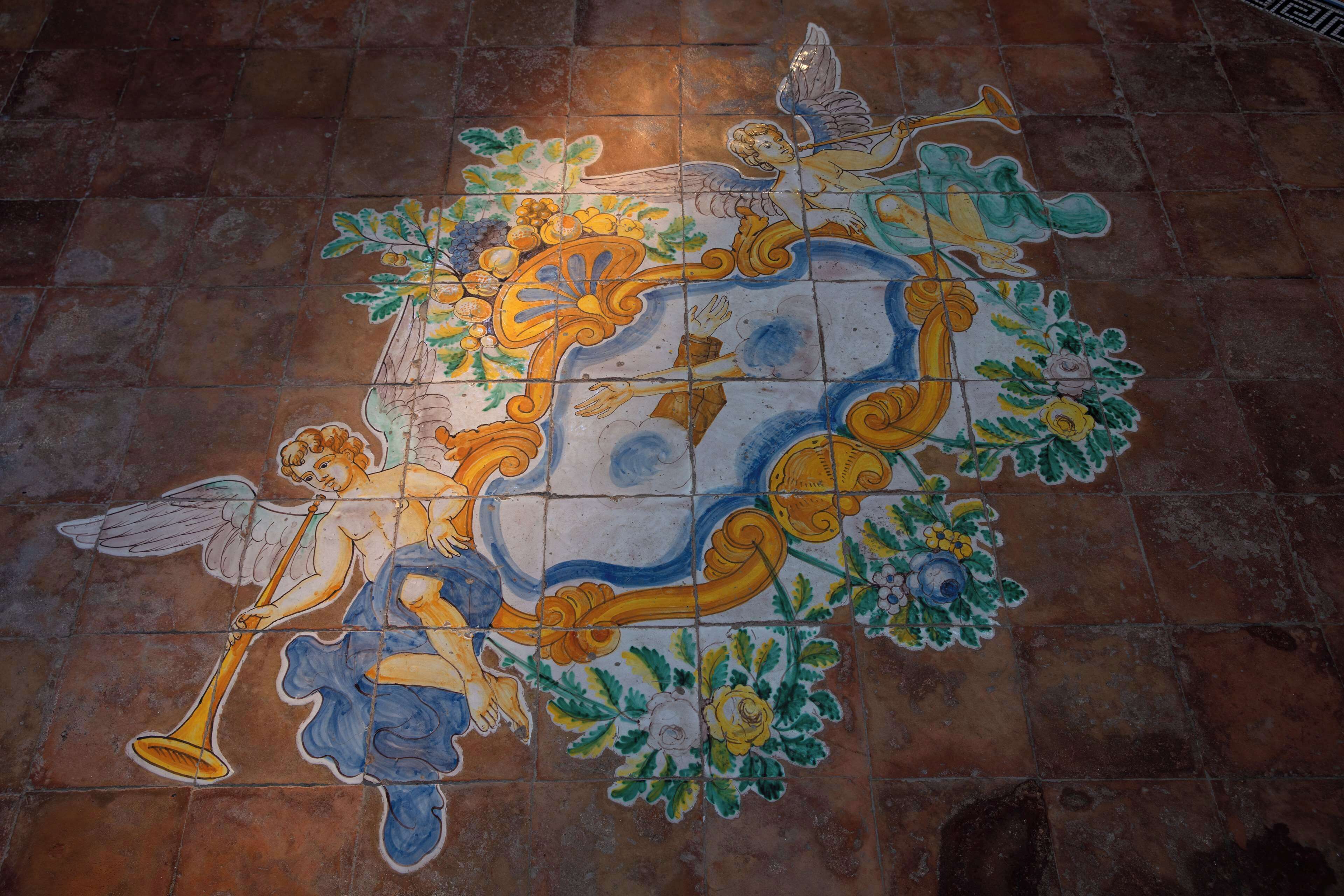 Un detallado mosaico con figuras angelicales y motivos florales sobre un suelo de baldosas.